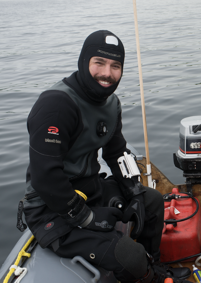 A man in diving gear sits on the back of an inflatable boat. 
